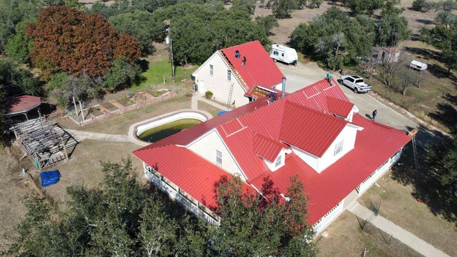 Crew installing a red metal roof on a ranch home with dormers and a wraparound porch