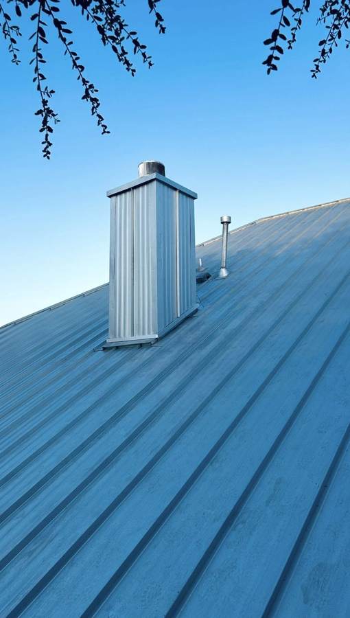 Metal-clad chimney chase and flashed vents on a metal roof