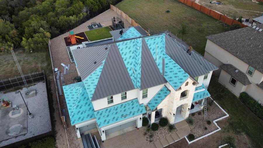 Gray standing seam panels going on over new underlayment on a two-story home